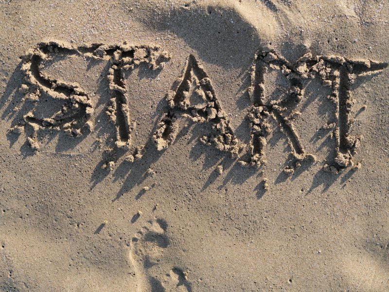 Text start written in sand on sea beach and bare footprints facing the word.